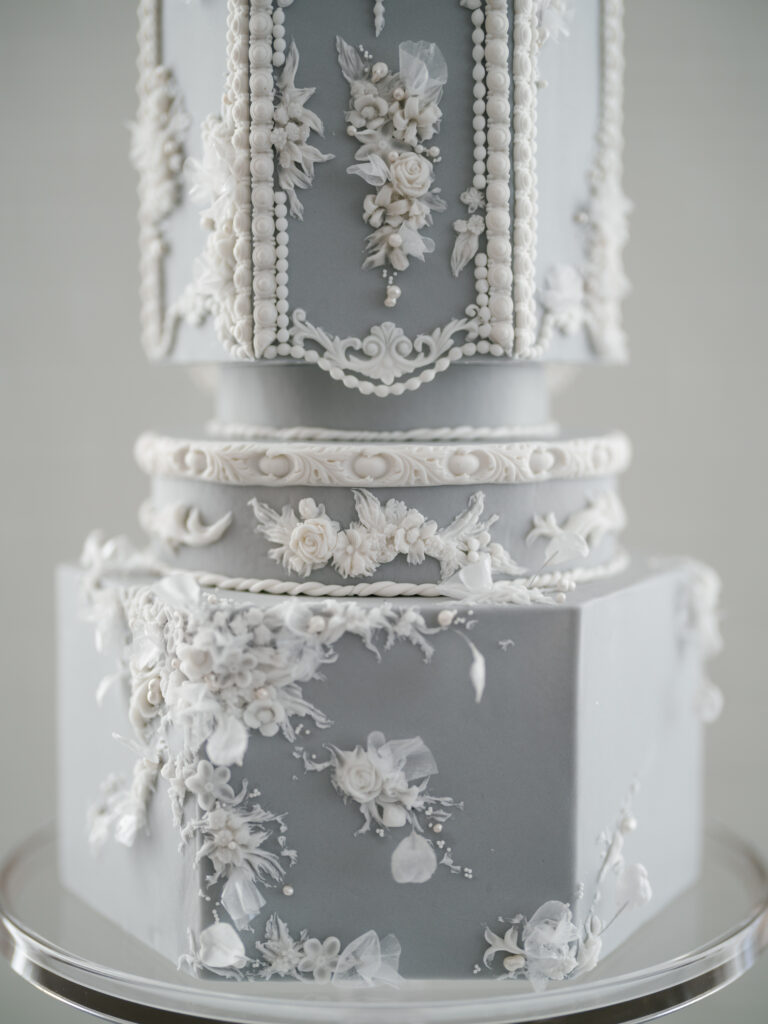 Close up view of a tiered wedding cake, with a grey blue fondant and intricate white icing