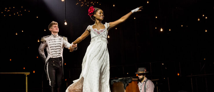 a woman in a long white dress reaching stage left while holding the hand of a man dressed in a white uniform