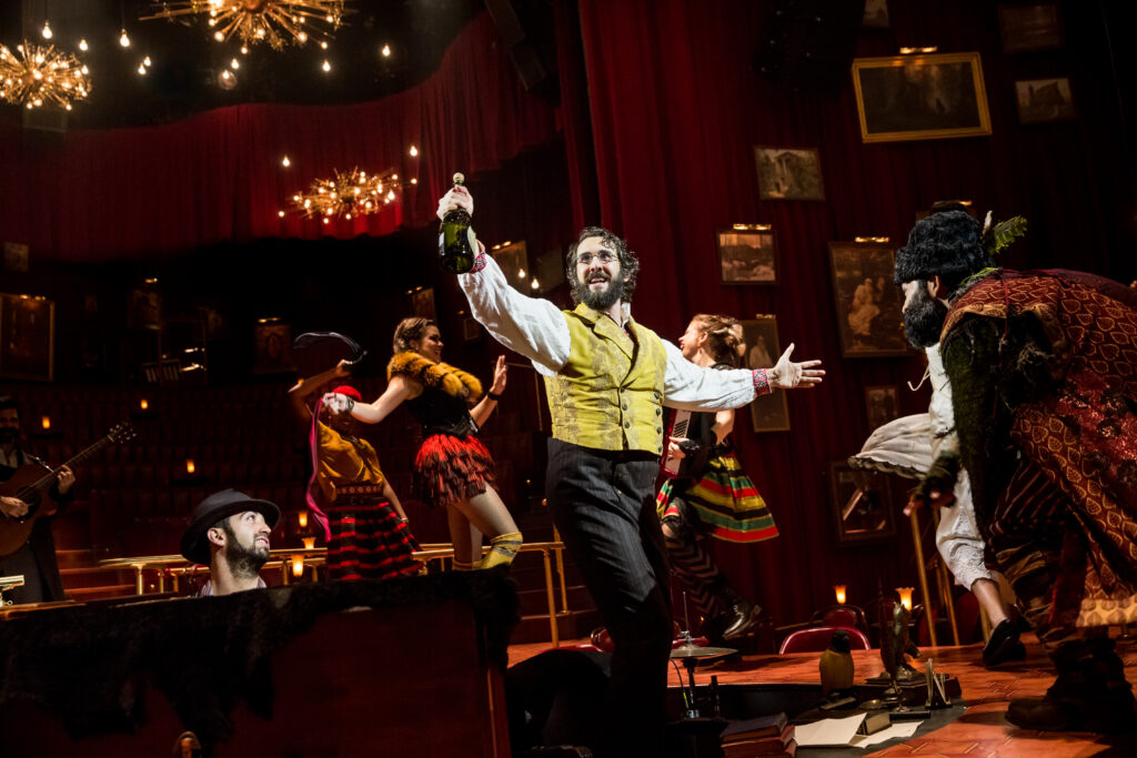 a male performer holding a bottle and moving around other performers on stage