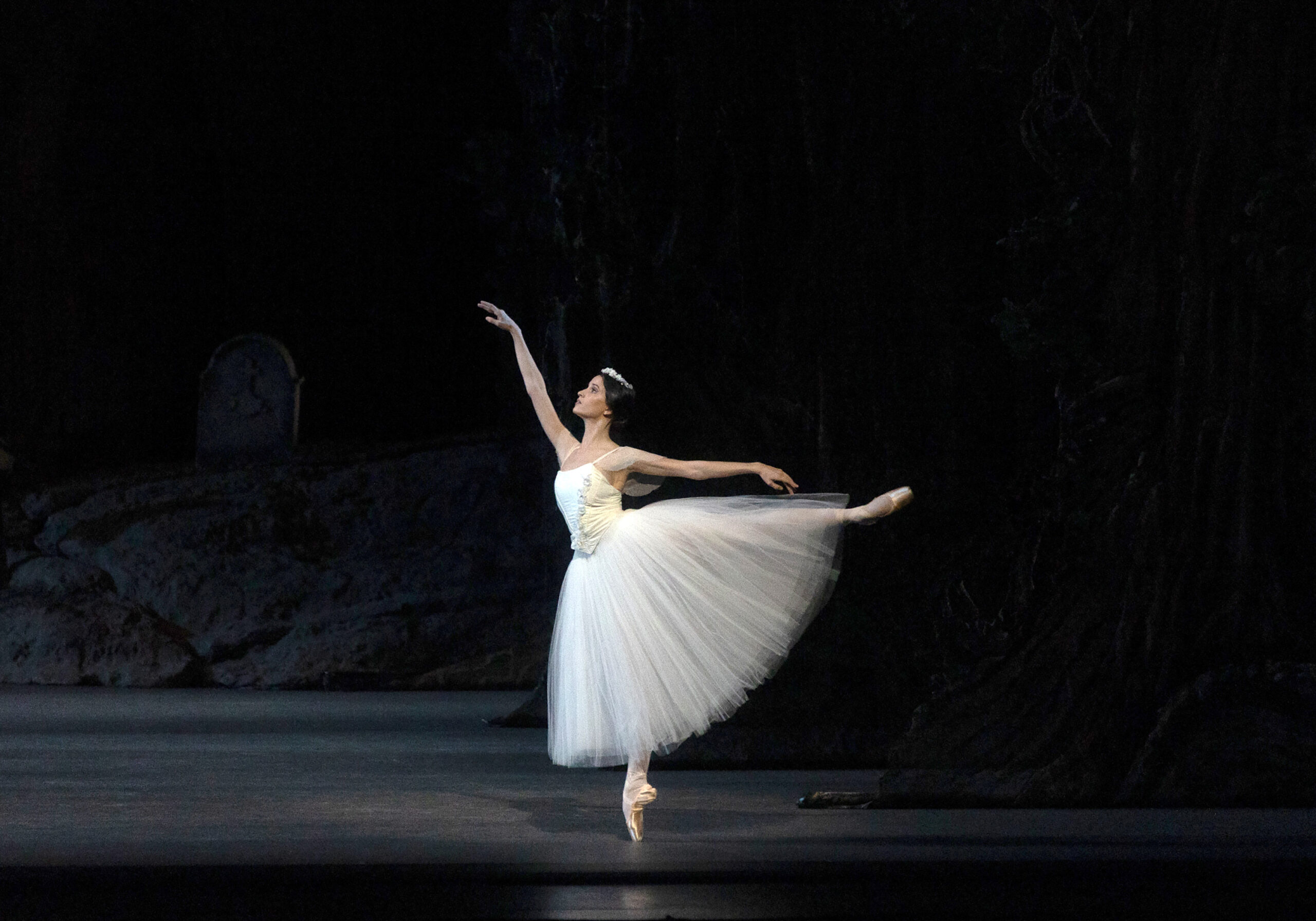 a female dancer wearing a long white tutu performing in first arabesque on stage