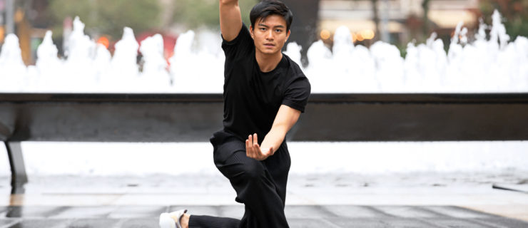 Chun Wai Chan kneels in front of Lincoln Center's fountain, one arm en en haut, and the other curved in front of his torso.