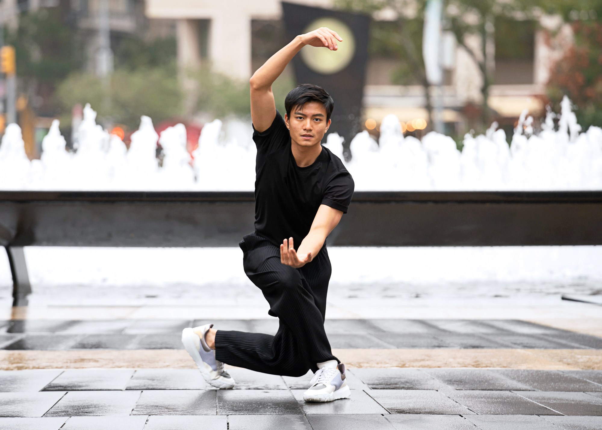 Chun Wai Chan kneels in front of Lincoln Center's fountain, one arm en en haut, and the other curved in front of his torso.