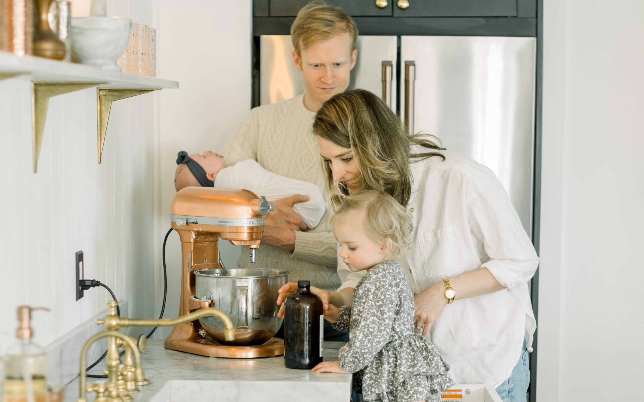 A man holding a baby, a woman and a child hulge over a kitchen mixer