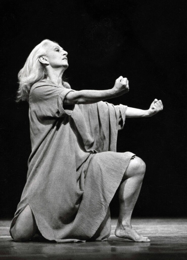 a female dancer wearing a tunic while kneeling with hands outstretched in fists