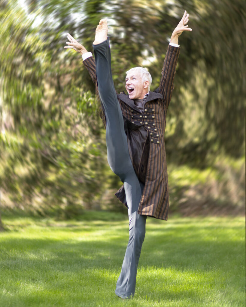 a performer wearing a brown coat and black pants kicking their leg above their head