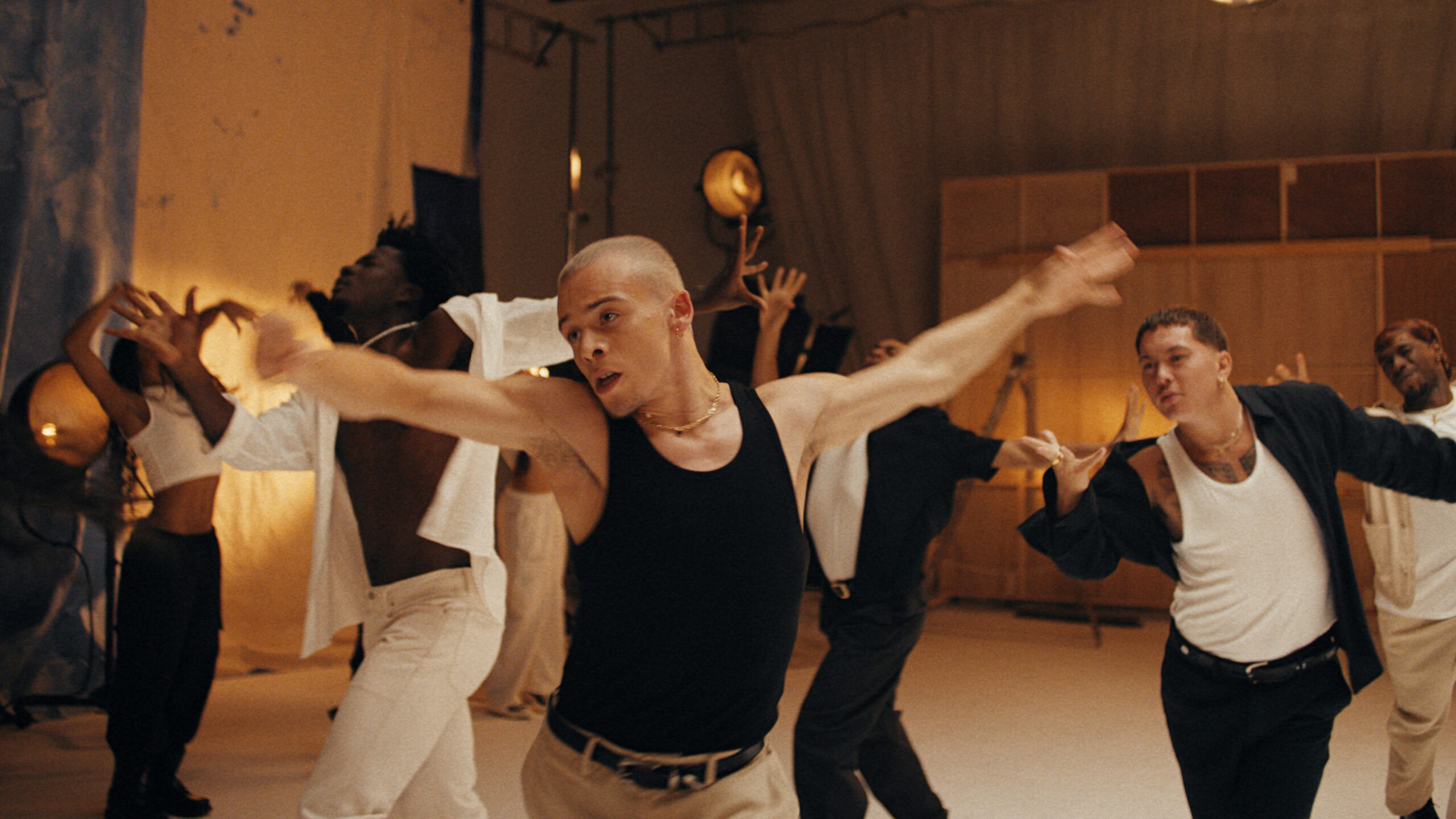 a male dancer with his arms spread wide to the side while dancing in a room with other performers