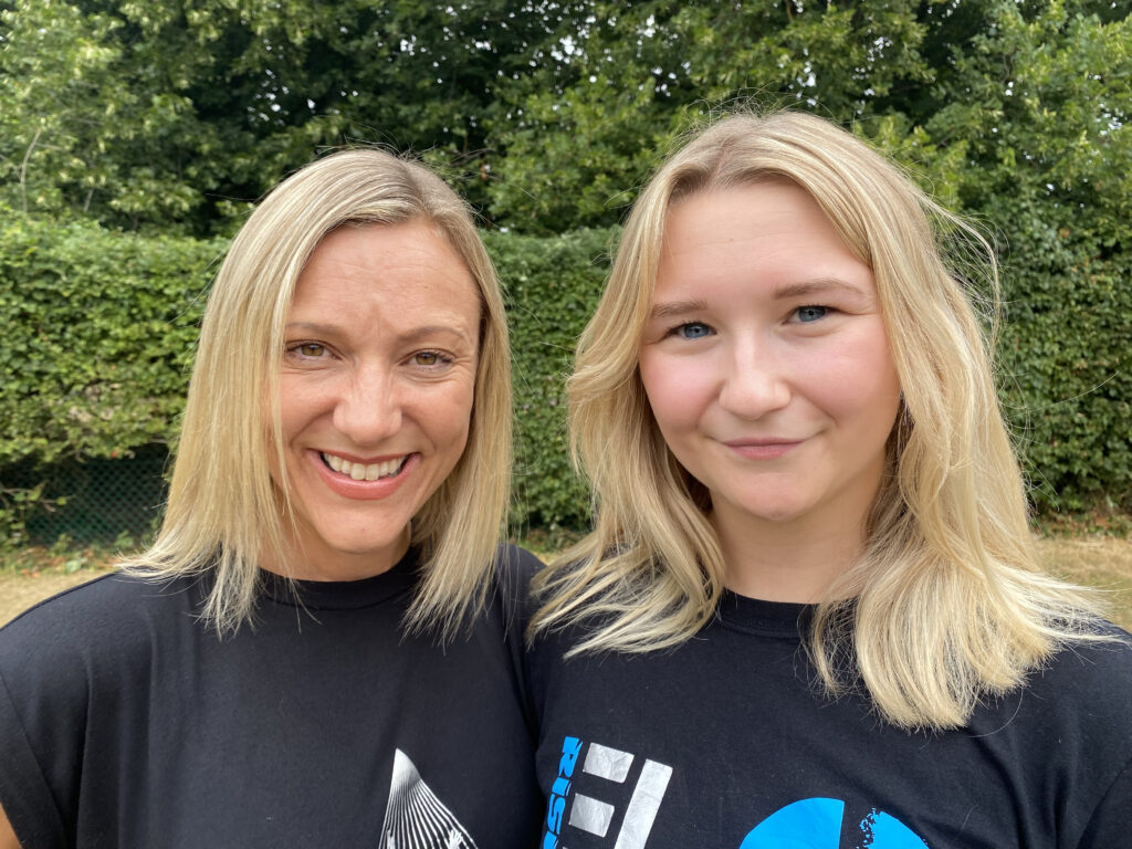 Two blonde women smiling at the camera while standing outside 