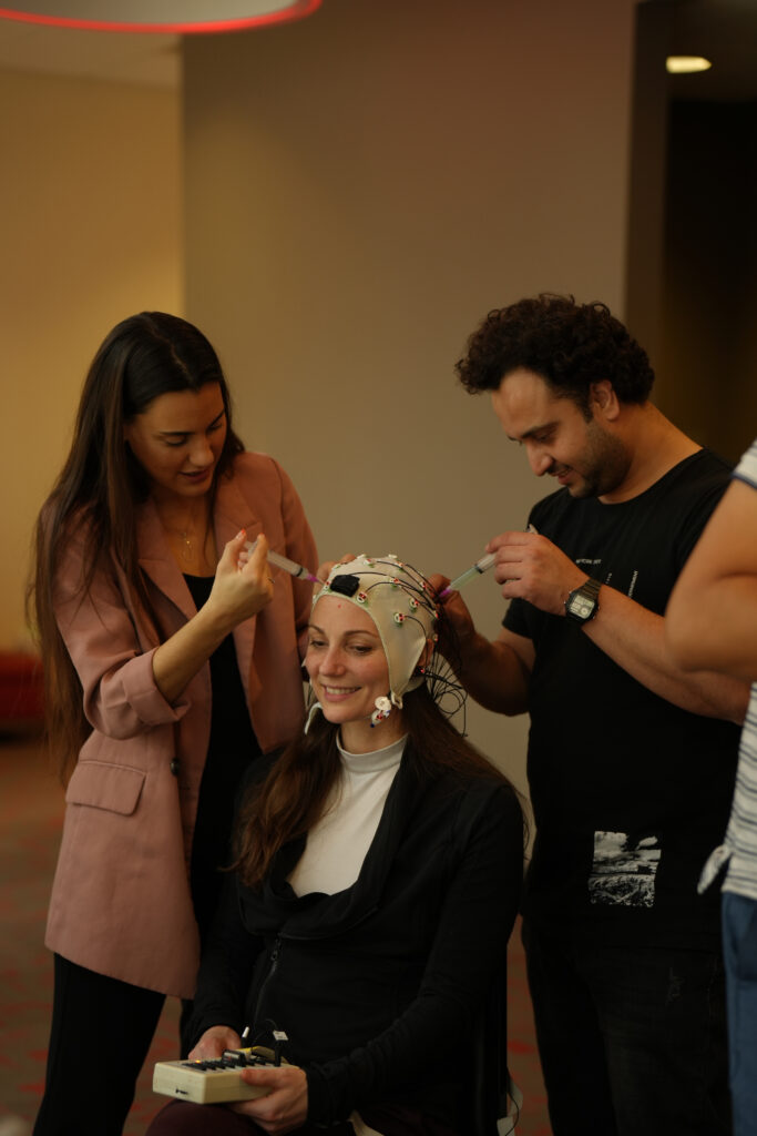 a woman wearing a cap with wires attached getting injected by another woman and man