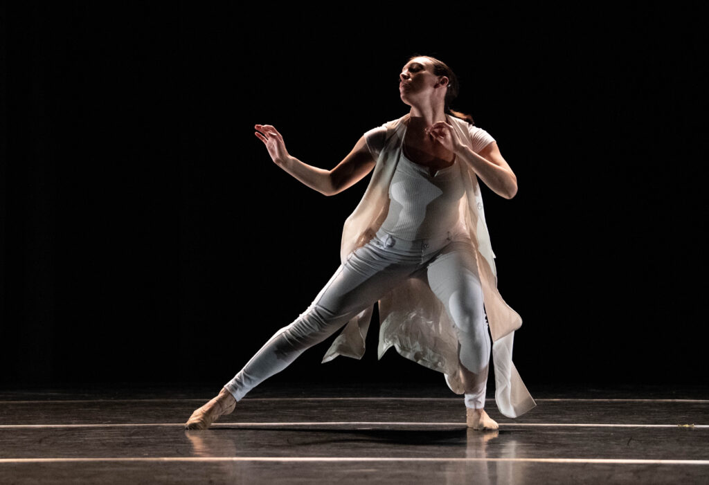 a female dancer wearing white dancing on a dimly lit stage