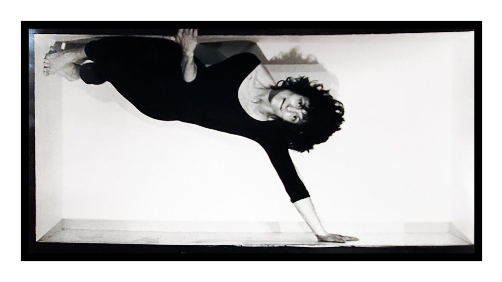 a female dancer in small box, supporting herself with one hand