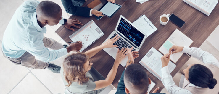 a group of people sitting around a table with laptops and notebooks