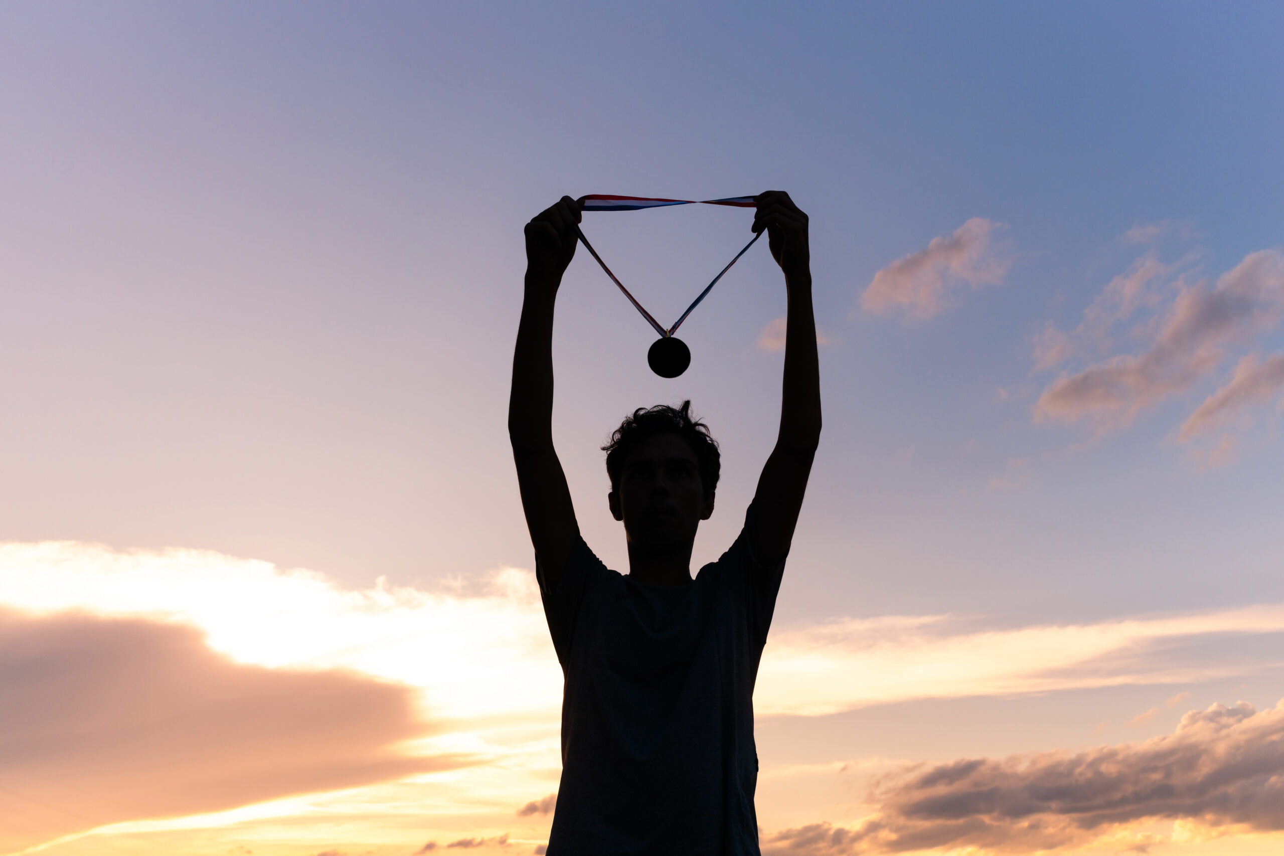 Silhouette of an athlete celebrating the gold medal against a sunset sky adorned with golden clouds in the background.