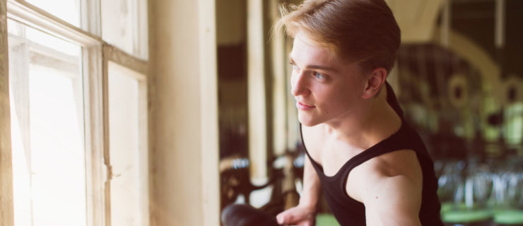 Male ballet dancer stretching at ballet barre, close-up of foot