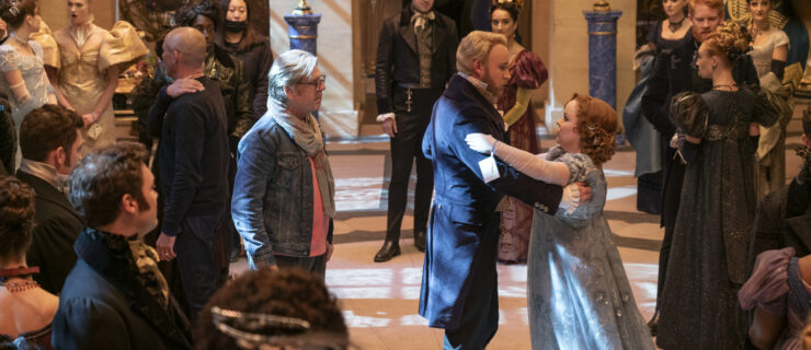 a male choreographer watching a couple dance in a ballroom