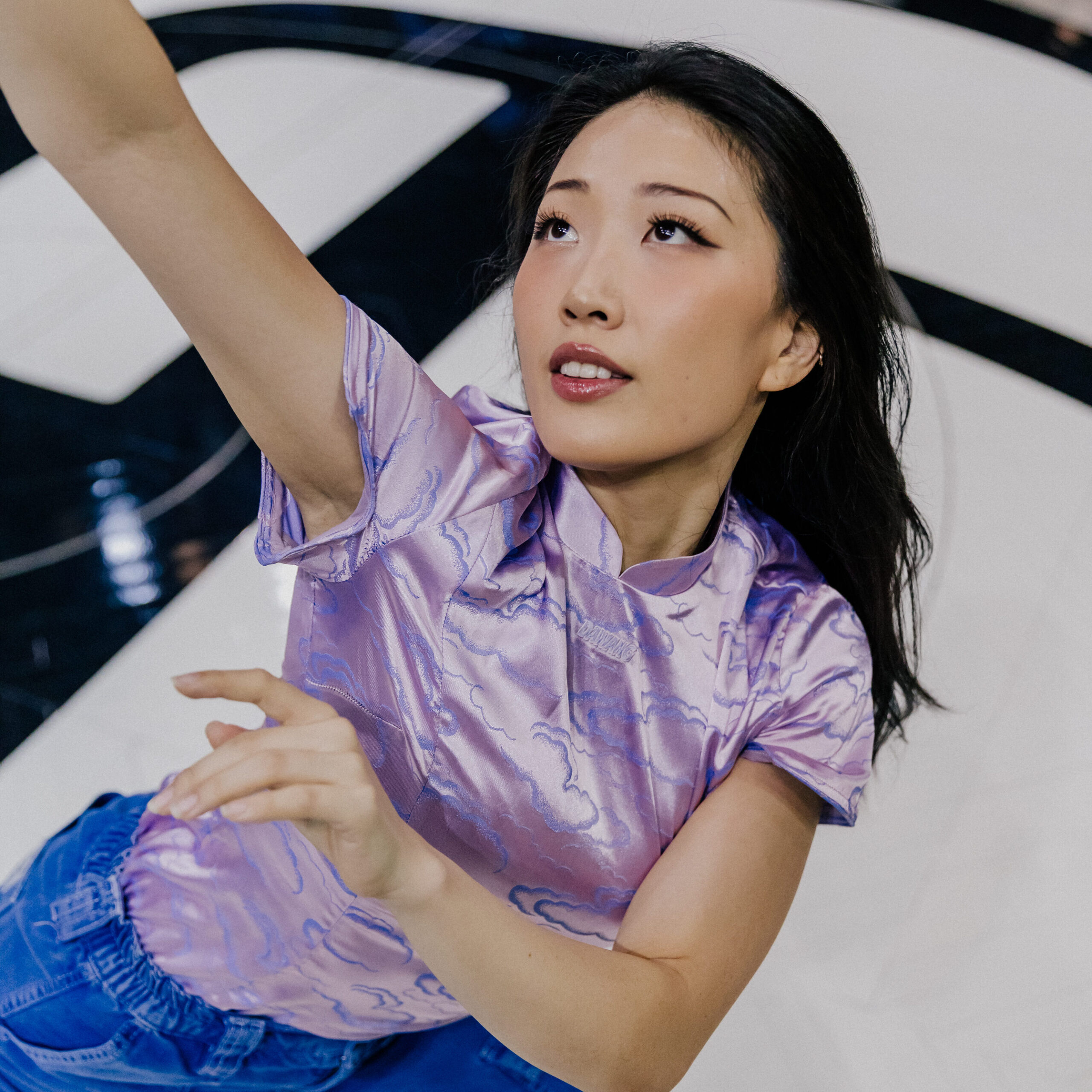 a female dancer wearing a purple top and jeans dancing in the middle of a basket ball court 