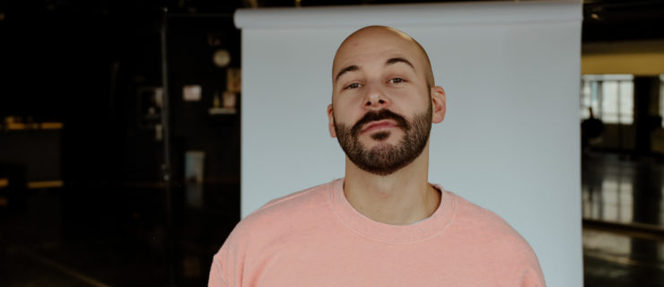 Closeup of Sam Chouinard, bearded, head tilted up, in front of a white backdrop