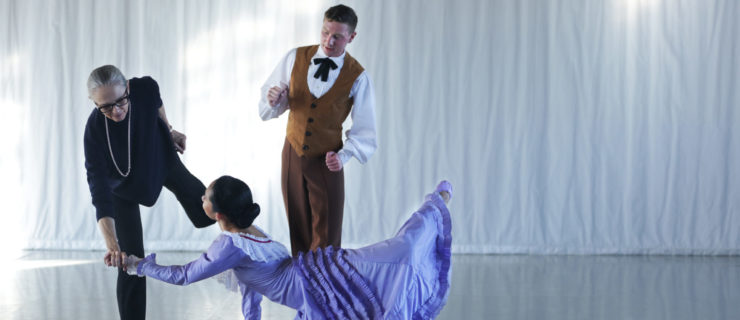 Woman in purple dress kneeling on floor, man and woman standing next to her