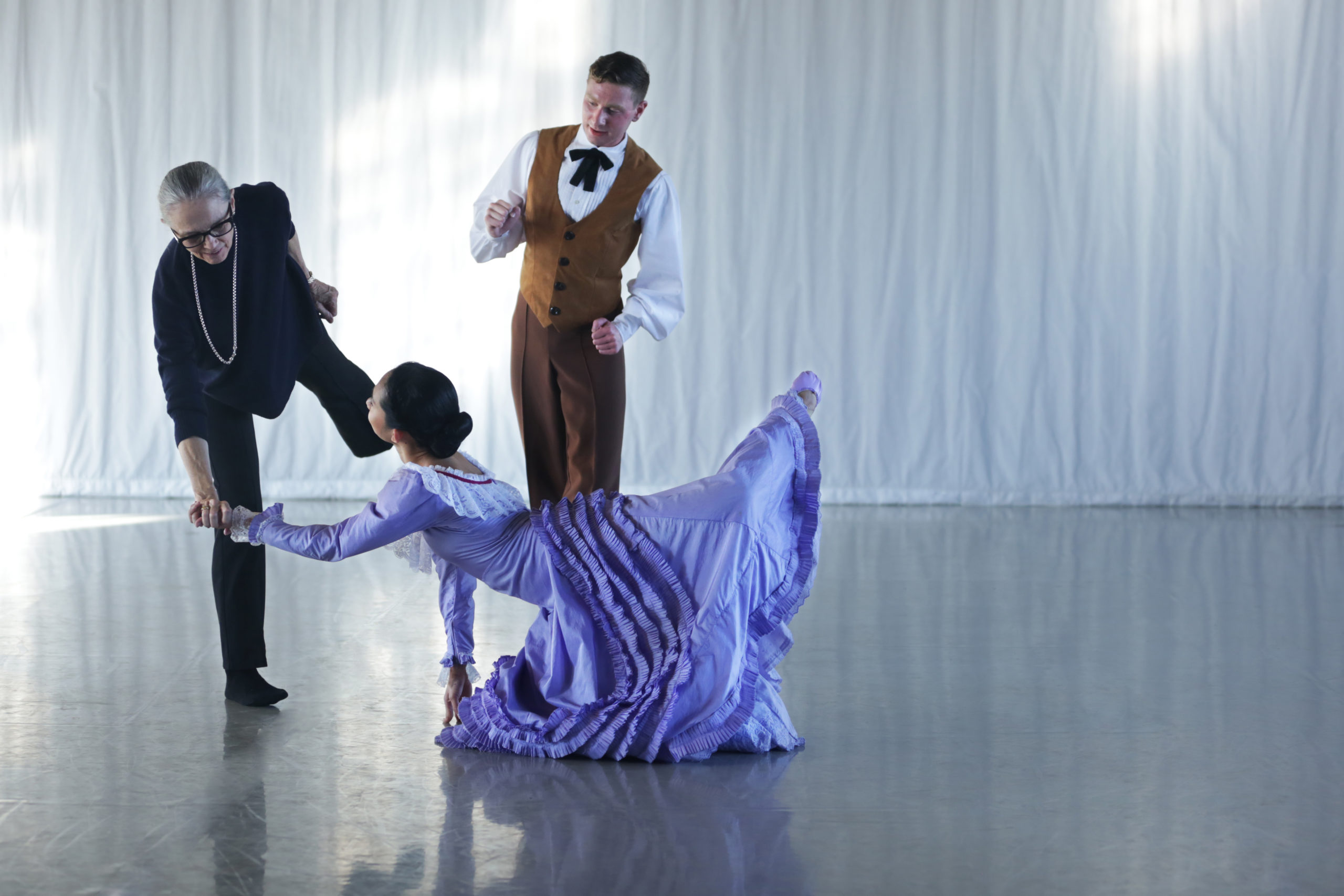 Woman in purple dress kneeling on floor, man and woman standing next to her