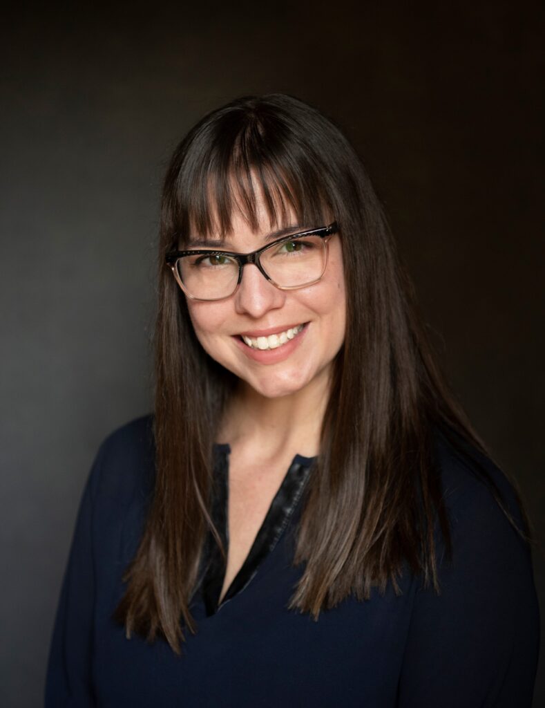 a woman with glasses and dark brown hair smiling at the camera 