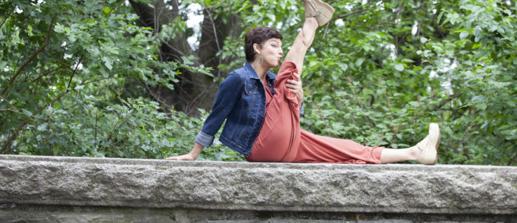 Amy Jordan sits atop a stone wall, her right leg extended upwards as she leans in to kiss her knee.