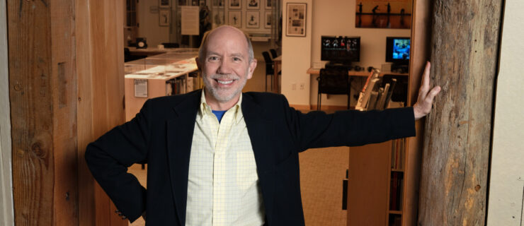 a man smiling at the camera with one hand against the wall