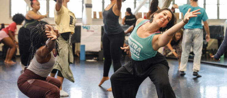 two female dancers mirroring each other while lunging side and reaching long with their arms