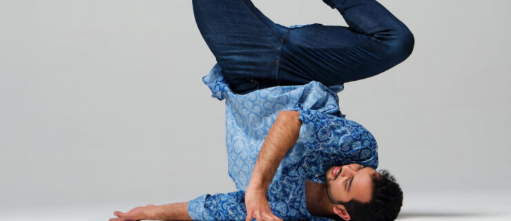 a male dancer performing a shoulder stand against a white backdrop