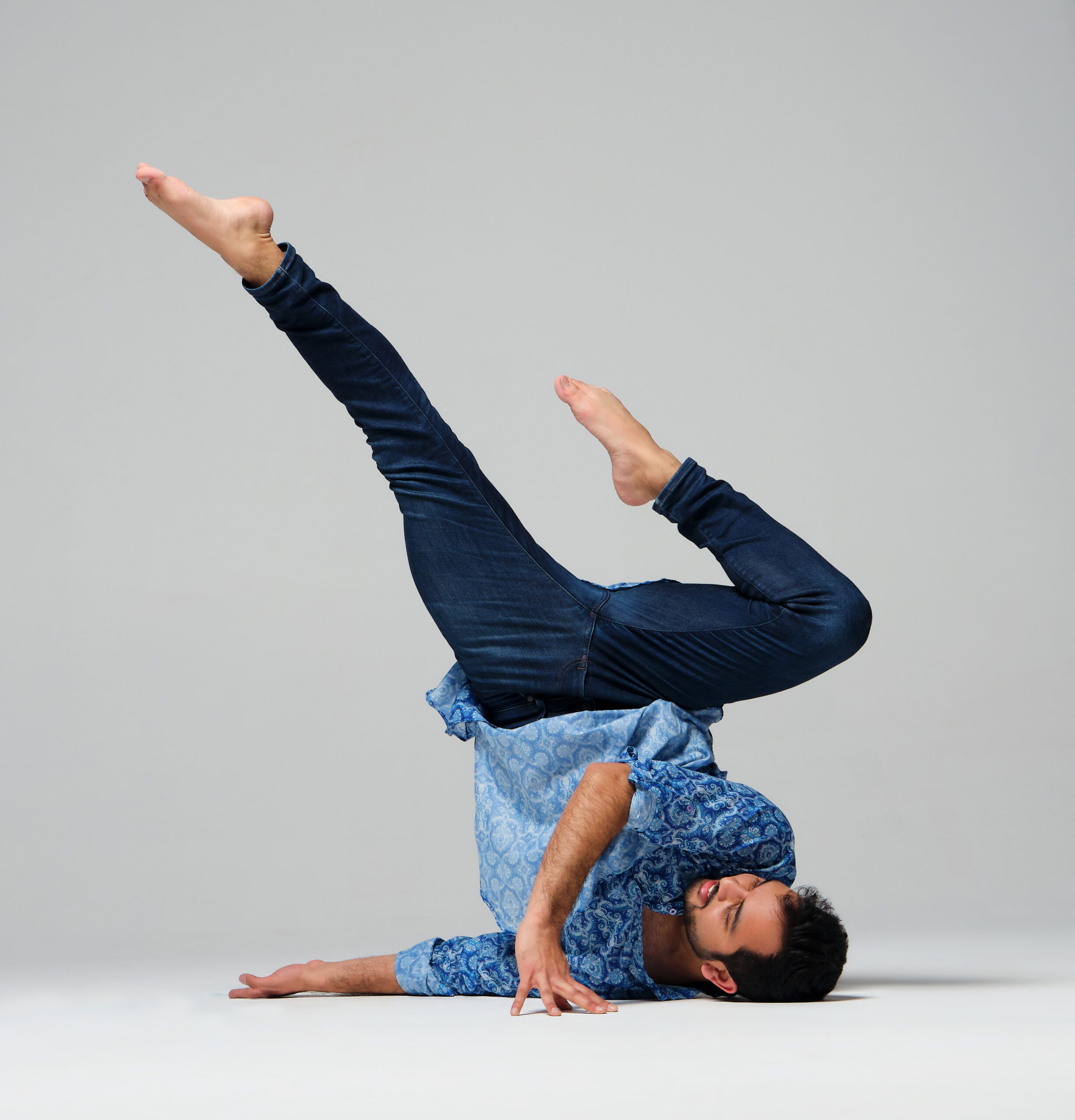 a male dancer performing a shoulder stand against a white backdrop