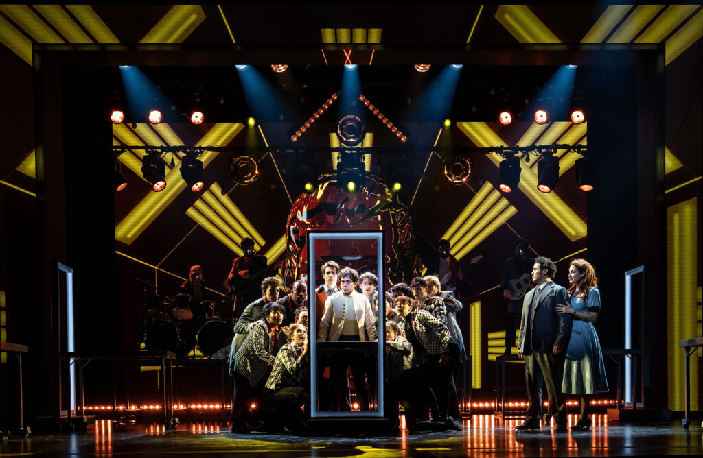 a group of performers on stage huddled around an open doorway looking towards the audience 