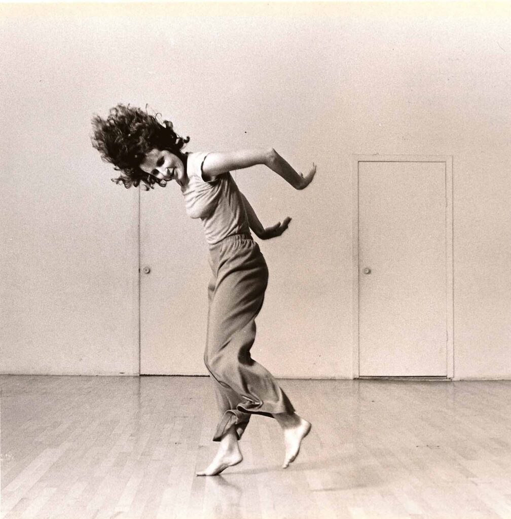 a female dancer swinging her arms back and hair flying in a large open studio