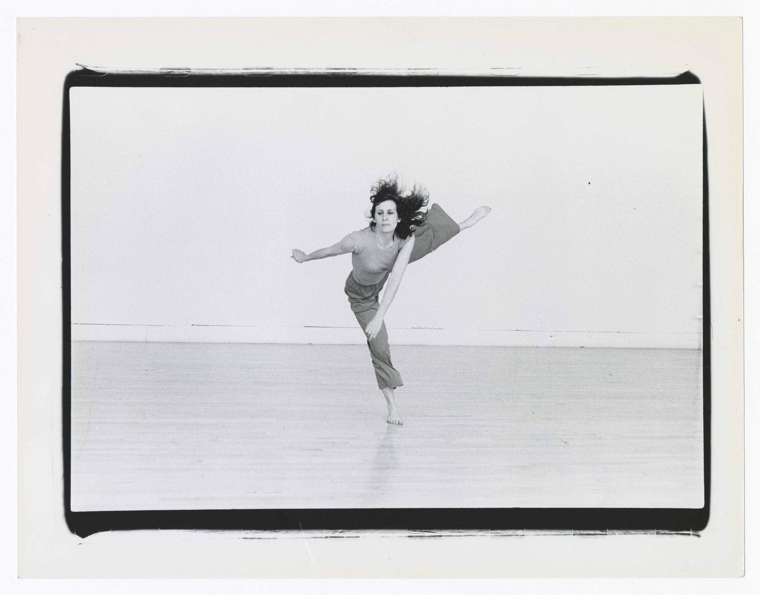 a female dancer in a black and white photo lifting her leg directly side and swinging her arms in opposition