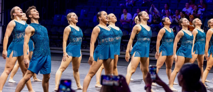 a group of dancers wearing blue standing tall on stage