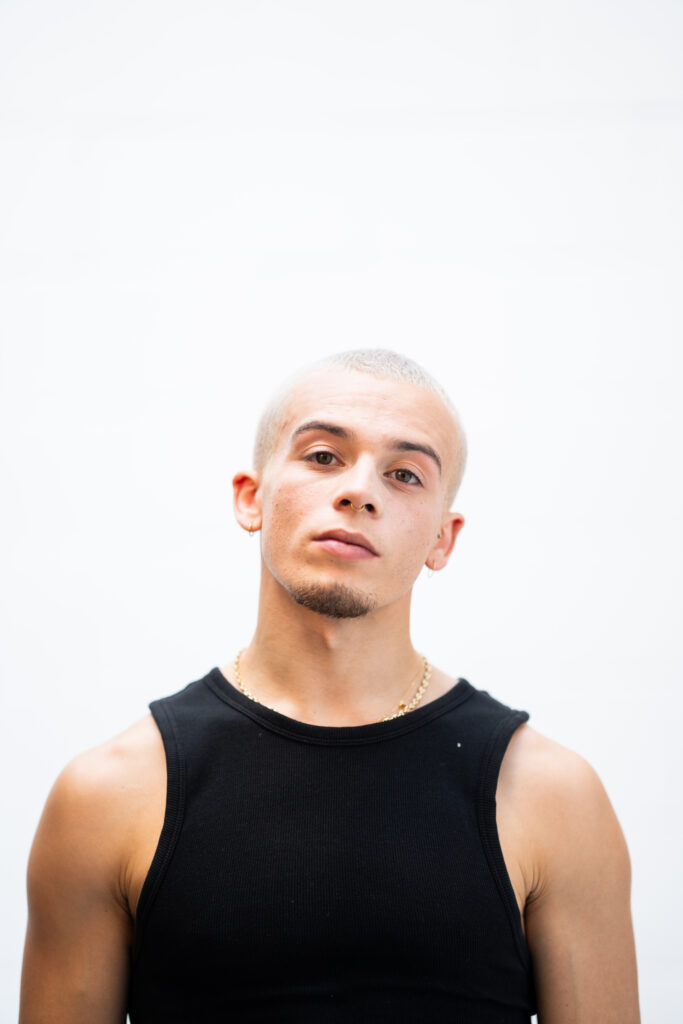 a male dancer wearing a black tank staring straight on towards the camera 