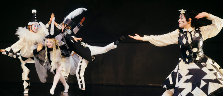 Four dancers in graphic black-and-white costumes and makeup perform in front of a black backdrop.