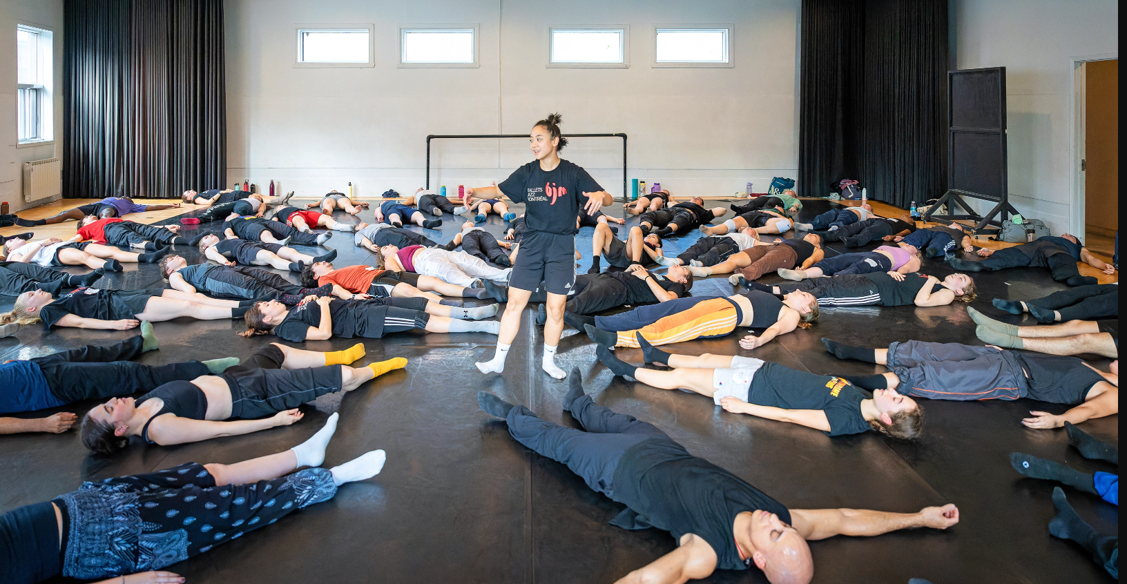 an instructor standing in the middle of a studio with students lying on their backs on the floor