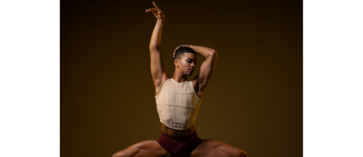 a male dancer on pointe posing in a wide second with one arm up