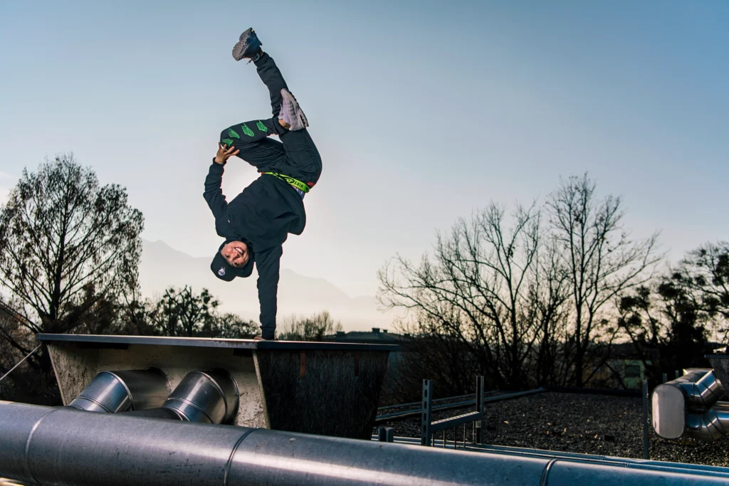 Sunny Choi poses on a rooftop near sunset. She is upside down, balanced on one hand. Her free arm grabs a bent knee as it pulls toward her torso; the other leg kicks up into the air.