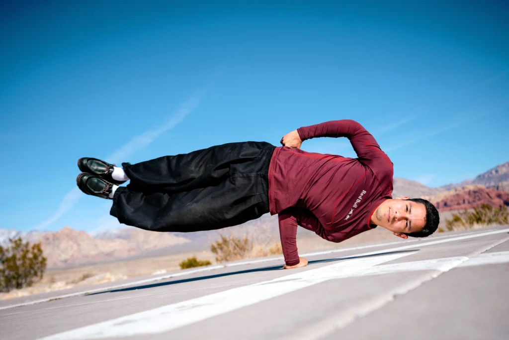 Victor Montalvo poses on a highway through the desert. He balances on one hand, body parallel to the ground, head inches from the pavement.